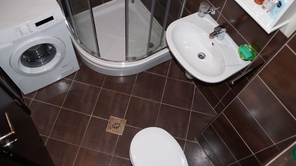 Kupatilo u stanu u Budvi, Crna Gora: tuš kabina, lavabo i veš mašina, braon pločice.