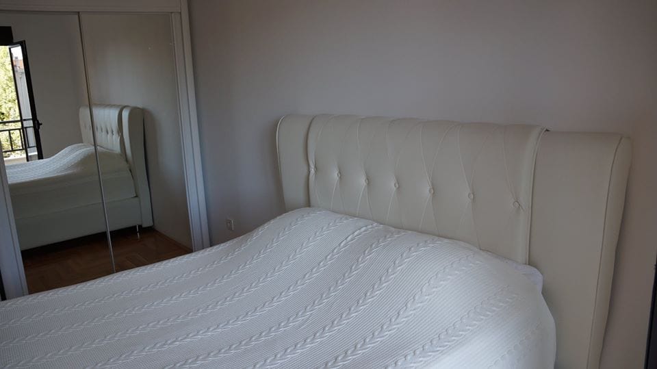 Svetla spavaća soba sa bračnim krevetom i ormarom sa ogledalom u stanu, Budva, Crna Gora.