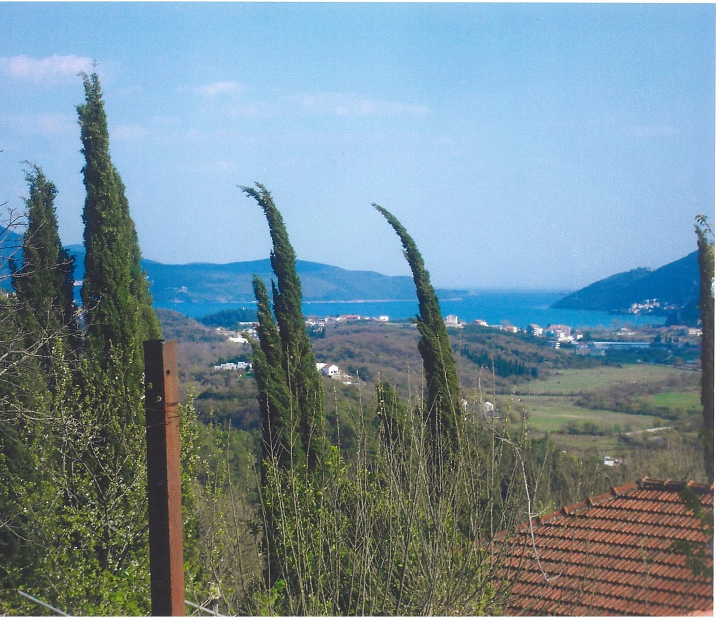 Panoramic view of the sea and mountains from a plot of land in Lučići, Herceg Novi, Montenegro: cypress trees and a tiled roof.
