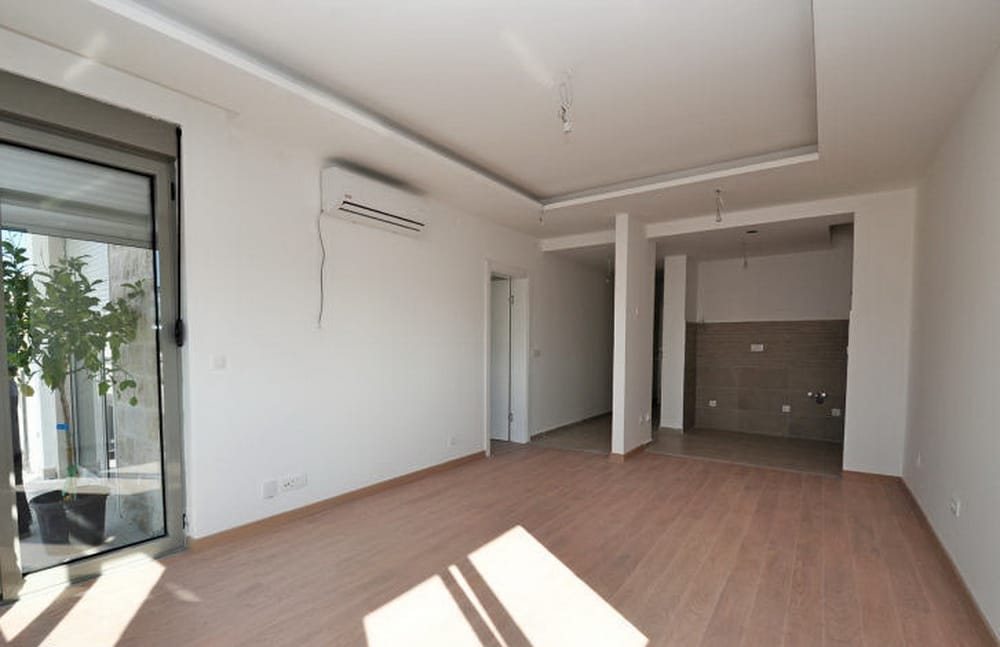 Jasny salon z laminatem i klimatyzacją w nowym kompleksie mieszkaniowym w Tivacie, Czarnogóra, widok na taras.