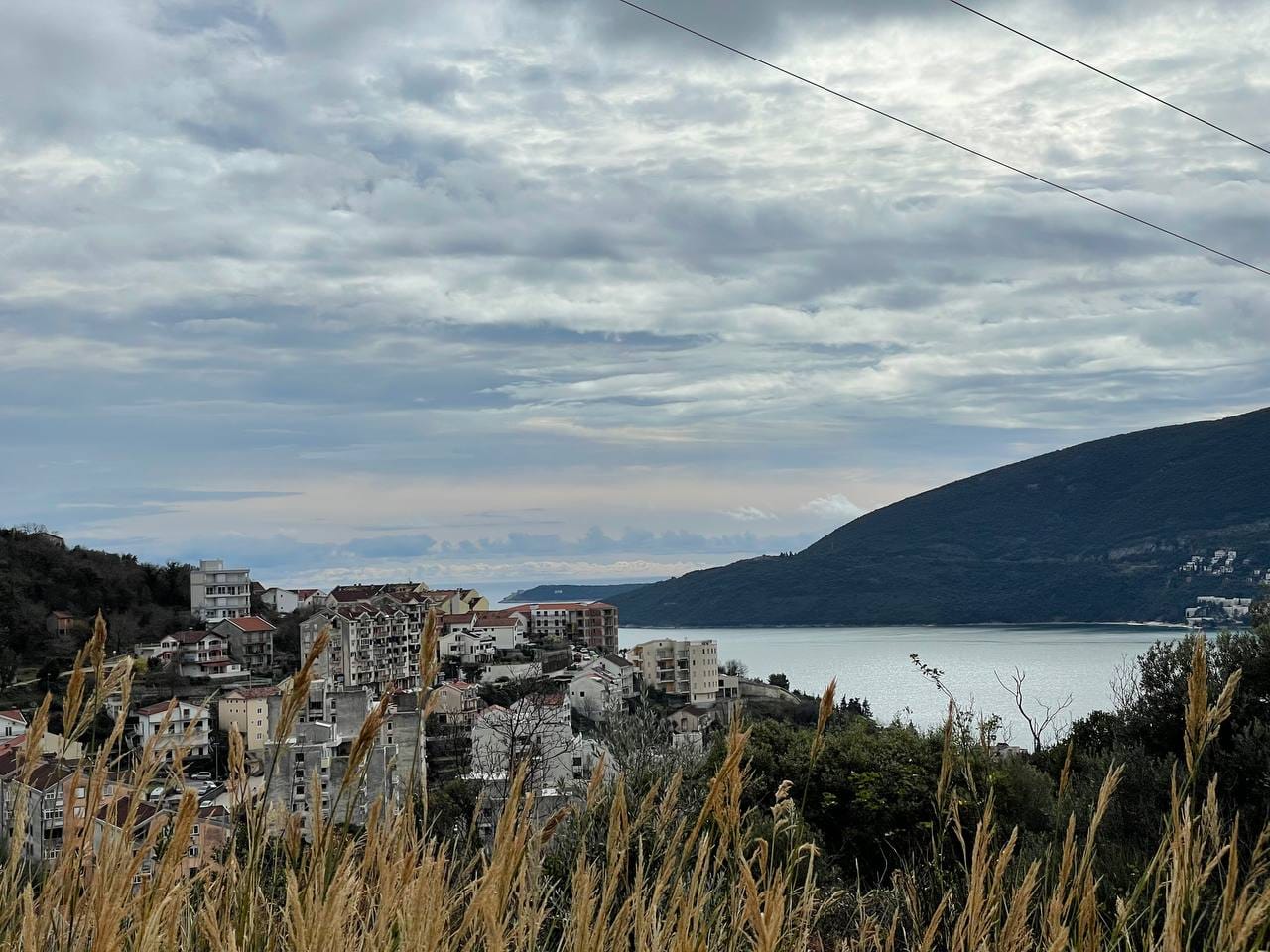 Panoramablick auf das Meer und die Stadt Herceg Novi, Montenegro, vom Grundstück Nr. 1519 vor dem Hintergrund von Bergen und einem bewölkten Himmel.