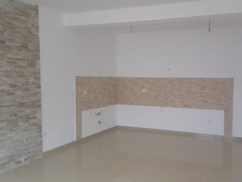Küche in einer Wohnung in Dobrota, Montenegro: helle Wandverkleidung aus dekorativem Stein und Fliesenboden, Bereich für die Küchenzeile.