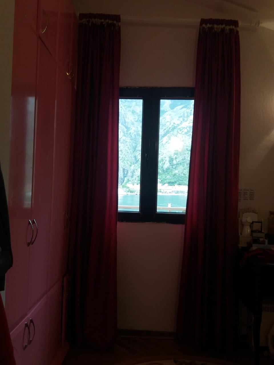 Schlafzimmer mit roten Vorhängen und Blick auf die Bucht von Kotor und die Berge in einem Haus in Muo, Montenegro.