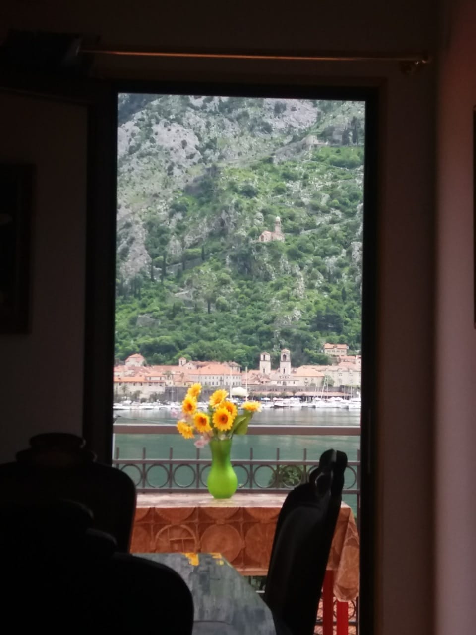 Blick aus dem Wohnzimmer eines Hauses in Muo, Montenegro: Panorama der Bucht von Kotor, der Berge und der Altstadt von der blumengeschmückten Terrasse.