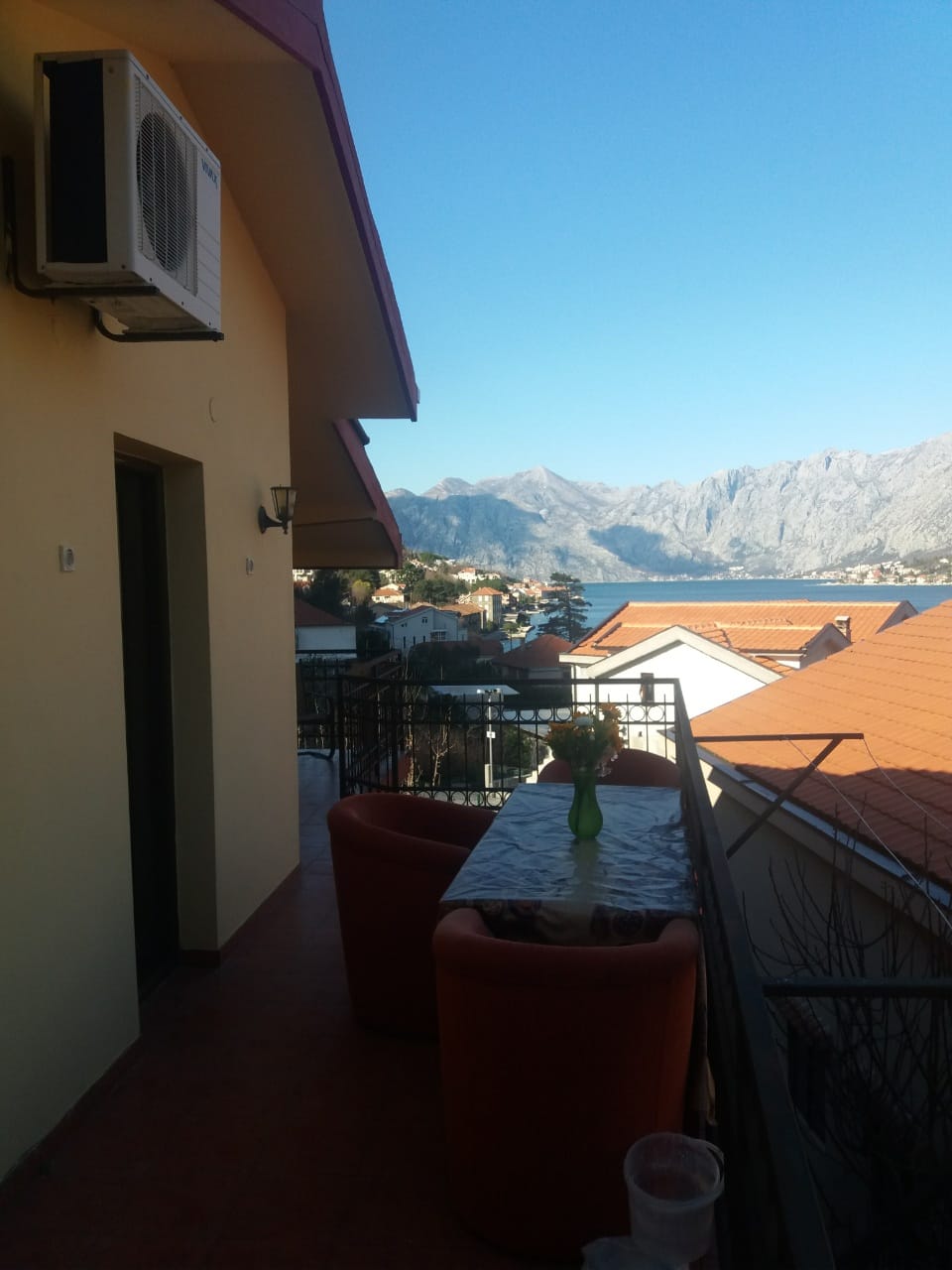 Balkon eines Hauses in Muo, Montenegro, mit Möbeln, Blick auf die Bucht von Kotor und die Berge, Terrakottafliesen und Ziegeldächer.