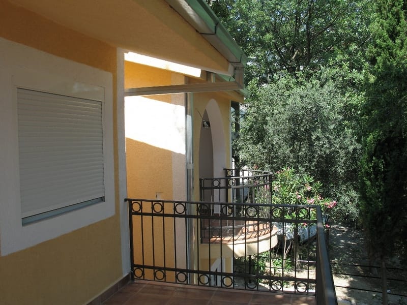 Balcony with wrought-iron railing and a view of the garden in a private house, Sutomore, Montenegro. Facade finished with yellow plaster.