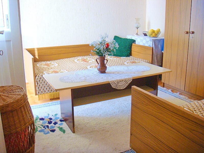 Innenraum des Wohnzimmers in einem Haus in Baošići, Montenegro: Holzmöbel, Sofa mit Überwurf und Teppich in hellen Tönen.