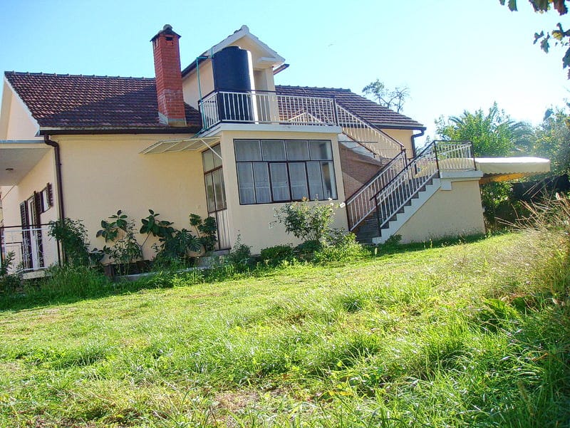 Zweistöckiges Haus mit Terrasse und Außentreppe in Baošići, Montenegro, umgeben von einem grünen Garten und Grundstück.
