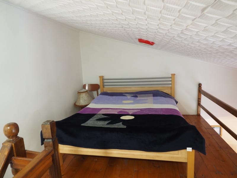 Spavaća zona na mansardnom spratu stana u gradu Bar, Crna Gora: bračni krevet, drveni pod i ograda.