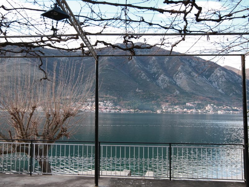 Vue depuis la terrasse de la maison à Dobrota, Monténégro : panorama de la baie de Kotor, montagnes et pergola de vigne au-dessus du balcon.