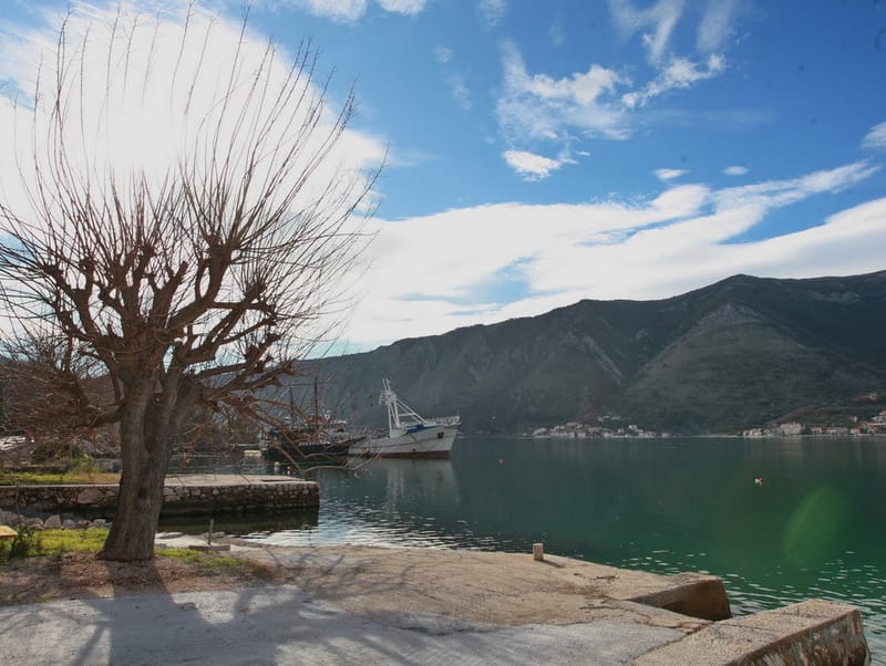 Vue sur la mer et les montagnes depuis le rivage près de la maison à Dobrota, Monténégro : quai, navires au mouillage et paysage de la baie.