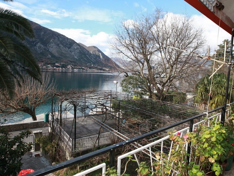 Vue depuis le balcon d’une maison à Dobrota, Monténégro : panorama de la baie de Kotor, montagnes et terrasse avec vignoble au bord de la mer.