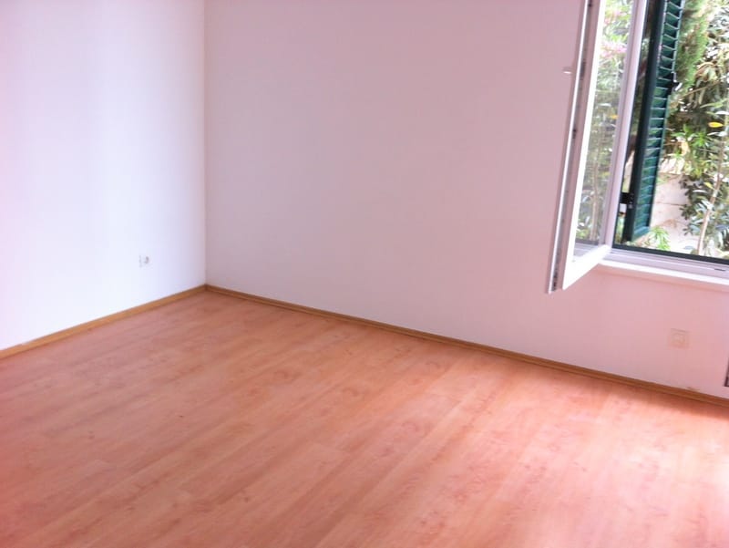 Chambre lumineuse avec parquet stratifié et fenêtre donnant sur une vue verdoyante dans un appartement à Herceg Novi, Monténégro.