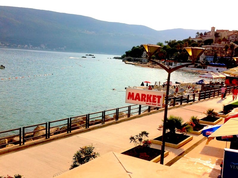 Vue sur la promenade, la plage et la mer à Herceg Novi, Monténégro : zone piétonne avec des palmiers et une boutique en bord de mer.