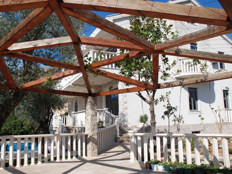 Wooden pergola on the terrace of a villa in Petrovac, Montenegro, overlooking the house facade and the garden pool.