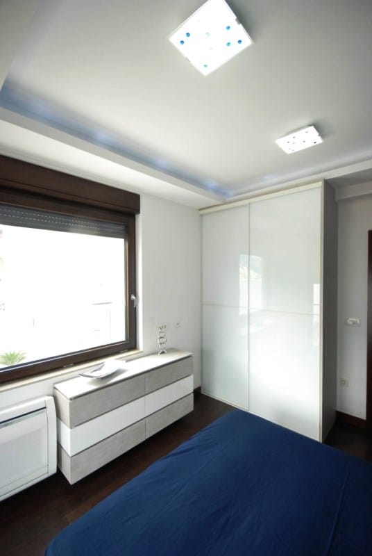 Modernes Schlafzimmer mit weißem Schiebetürenschrank und Kommode in einer Wohnanlage, Kostanica, Montenegro.