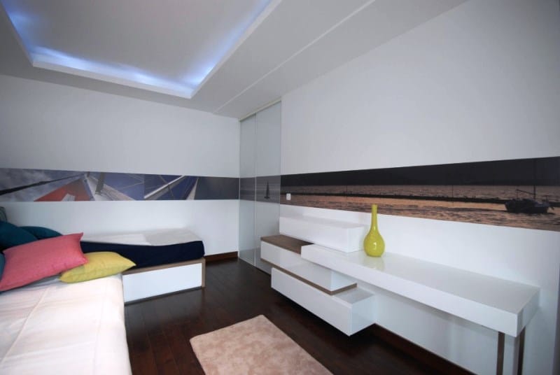 Modernes Schlafzimmer in der Wohnanlage Kostanica, Montenegro: weiße Möbel, dunkler Boden, Deckenbeleuchtung und maritimer Wanddekor.