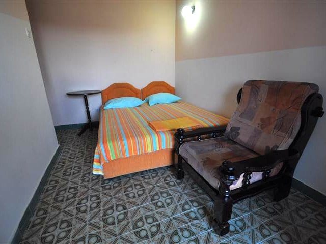 Bedroom in a house in Petrovac, Montenegro: double bed, armchair with wooden armrests, and tiled floor.