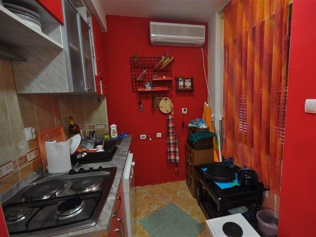 Compact kitchen with red walls, a gas stove, and air conditioning in a house for sale, Petrovac, Montenegro.