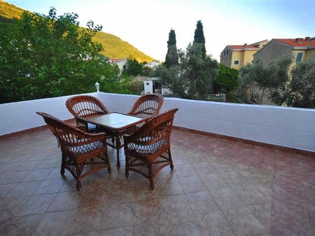 Open terrace with wicker chairs and mountain views in a house in Petrovac, Montenegro. Tiled floor, cozy seating area.