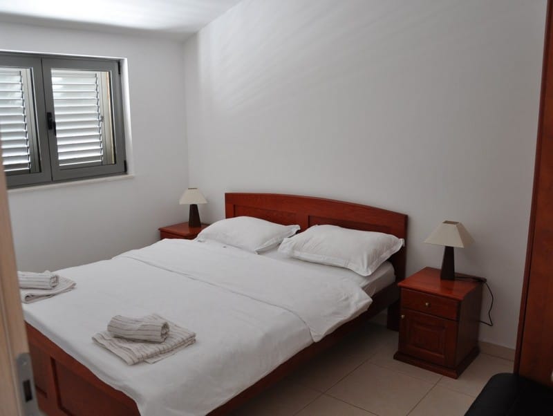 Chambre avec lit double et tables de chevet dans un appartement à Bečići, Monténégro. Finition claire et fenêtre.