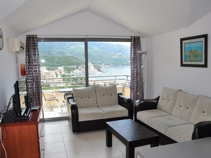 Salon dans un appartement à Bečići, Monténégro : vue panoramique sur la mer et les montagnes, mobilier clair, accès à la terrasse.