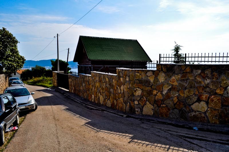 Grundstück in Šušanj, Bar Riviera, Montenegro: Blick auf eine Steinmauer und ein Haus mit grünem Dach an der Straße.