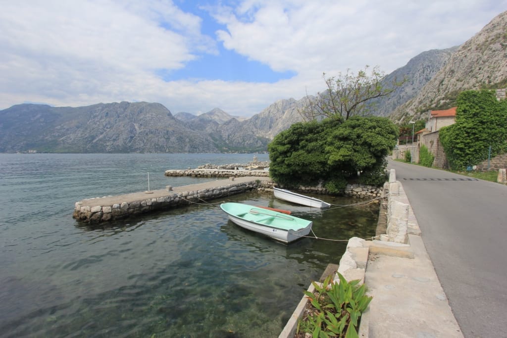 Vue sur la mer et le quai avec des bateaux près de la maison à Dobrota, Monténégro : promenade, montagnes et eau transparente de la baie.
