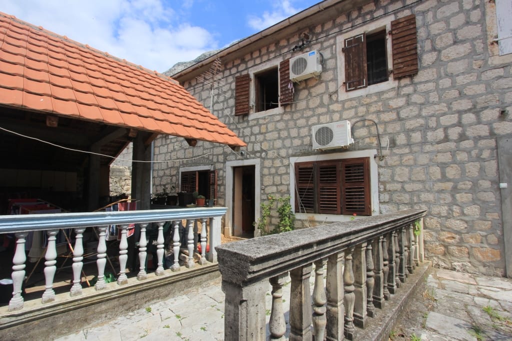 Maison traditionnelle en pierre avec toit en tuiles et terrasse à Dobrota, Monténégro : vue sur la façade et la cour intérieure.