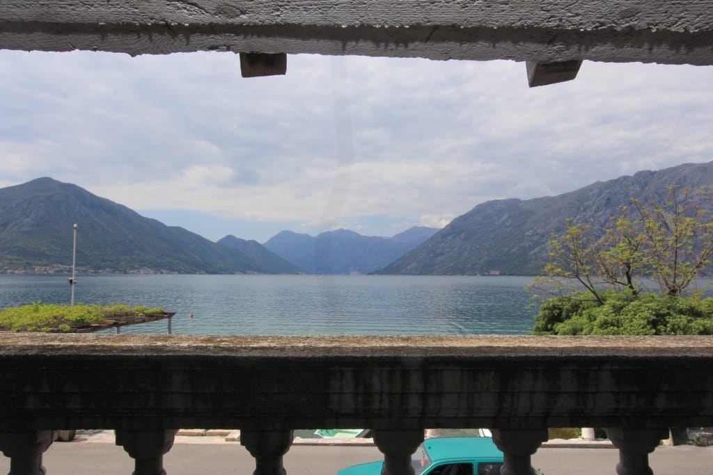 Vue depuis le balcon d’une maison à Dobrota, Monténégro : panorama de la baie de Kotor, montagnes et balustrade en pierre de la terrasse.