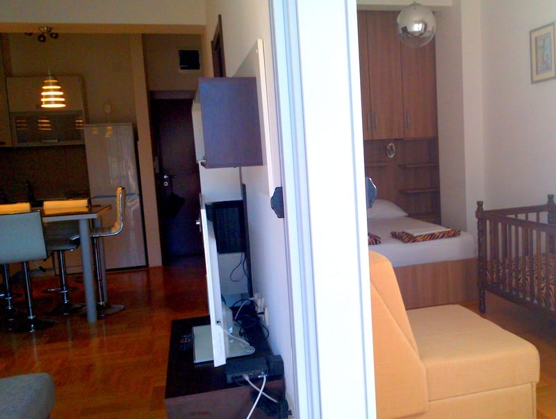 Innenraum einer Wohnung in Budva, Montenegro: offene Küche mit Bar und Schlafzimmer mit Bett und Kinderbett.