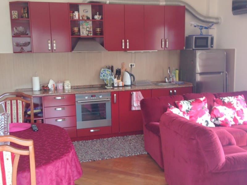 Kuhinja-dnevna soba sa crvenim nameštajem i mekom sofom u stanu na prodaju, Budva, Crna Gora.