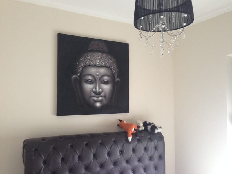 Schlafzimmerinterieur in einer Wohnung in Dobrota, Montenegro: Leder-Kopfteil des Bettes, ein Buddha-Gemälde und ein schwarzer Kronleuchter.