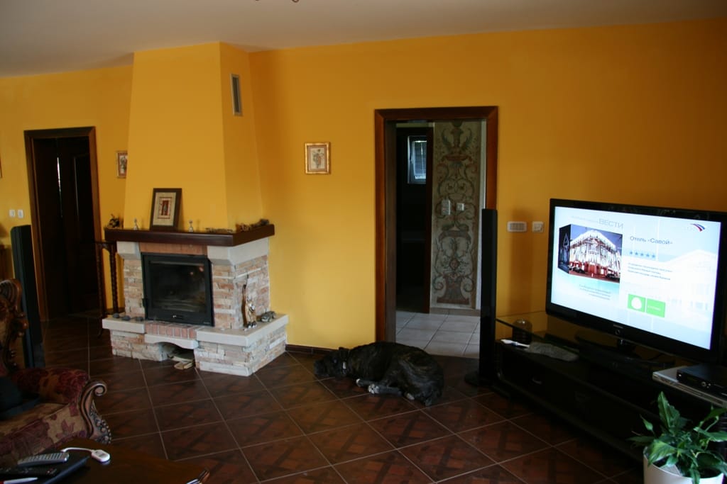 Salon dans un appartement à Radovići, Monténégro : cheminée en pierre, murs jaunes, sol carrelé et coin TV.