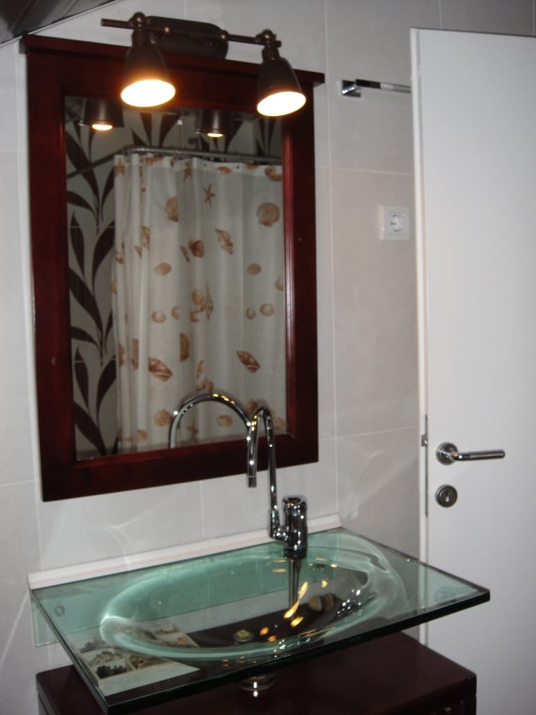 Salle de bains dans l’appartement, Radovići, Monténégro : lavabo en verre, miroir dans un cadre sombre et finition moderne.