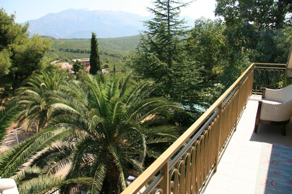 Balcon avec mobilier en osier et vue sur les montagnes et les palmiers dans un appartement, Radovići, Monténégro.