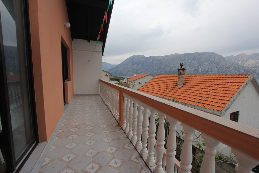 Balkon z balustradą w domu w Prčanj, Czarnogóra, z panoramicznym widokiem na góry i dachy z dachówki.