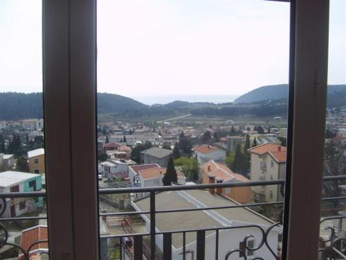 Pogled sa balkona stana u Sutomoru, Crna Gora: panorama grada, zeleni brežuljci i morski horizont u daljini.