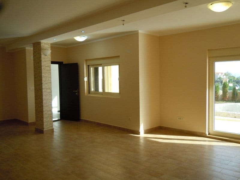 Spacious living room in a house in Budva, Montenegro: light finishes, tiled floor, decorative column, and access to the terrace.
