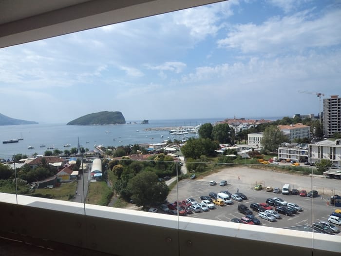 Pogled sa balkona stana u Budvi, Crna Gora: panorama mora, ostrva Svetog Nikole i gradski parking.