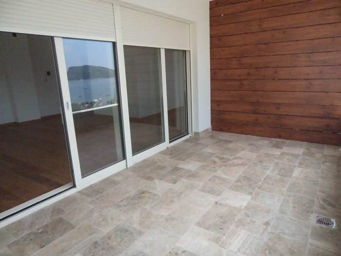 Prostran balkon sa kamenim podom i drvenom oblogom u stanu u Budvi, Crna Gora, sa panoramskim pogledom na more.