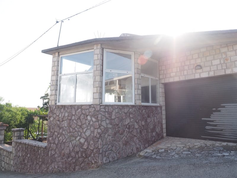 Fasada kuće u Šušnju, Crna Gora: kamena obloga zidova, panoramski prozori i garaža sa rolo vratima.