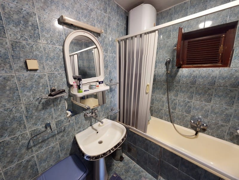 Kupatilo u kući, Šušanj, Crna Gora: pločice u plavim tonovima, umivaonik, kada sa zavesom i bojler.