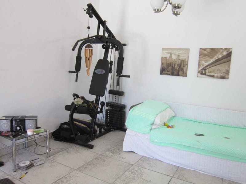 Chambre avec appareil de fitness et lit dans une maison à vendre à Uteha, Monténégro. Pièce lumineuse avec sol carrelé.