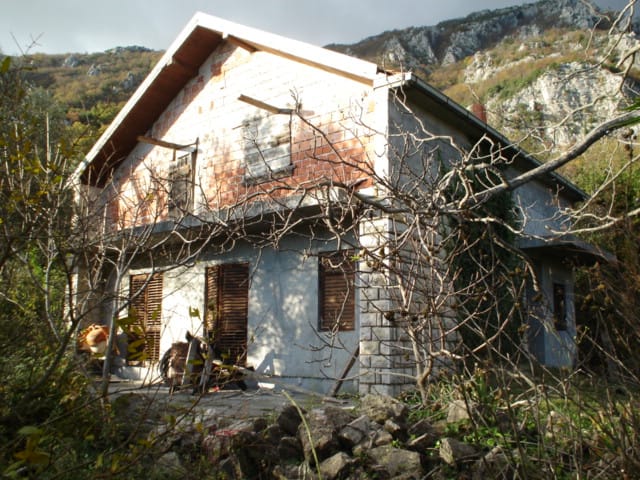 Zweistöckiges Haus zur Rekonstruktion auf einem Grundstück in Herceg Novi, Montenegro, vor Bergkulisse.