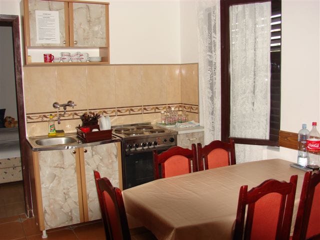 Kitchen with dining area in a house in Budva, Montenegro: stove, sink, wooden table, and chairs with red upholstery.