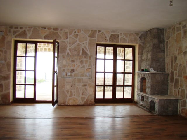 Living room with stone wall finishes and a fireplace in a house in Petrovac, Montenegro, with access to the terrace through panoramic doors