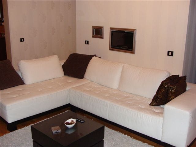 Bela ugaona sofa u modernom dnevnom boravku stana u Budvi, Crna Gora: stilizovan enterijer sa tamnim klub stolom.