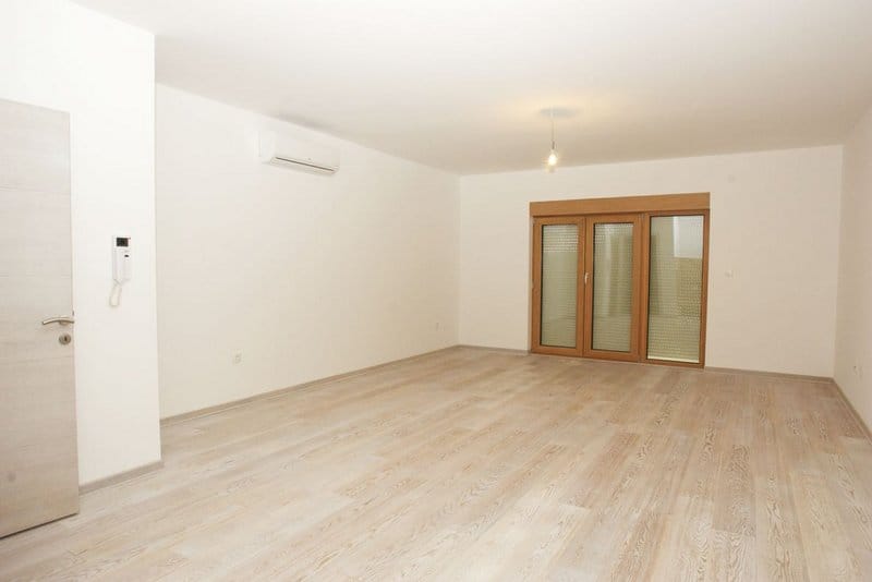 Svetla dnevna soba u stanu u Pržnu, Crna Gora: laminat u imitaciji drveta, beli zidovi, klima-uređaj i panoramska vrata.