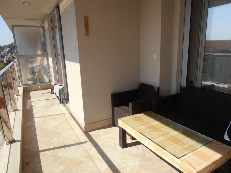 Prostran balkon sa pletenim nameštajem u stanu u Budvi, Crna Gora: pogled na grad, pločice na podu i panoramski prozori.
